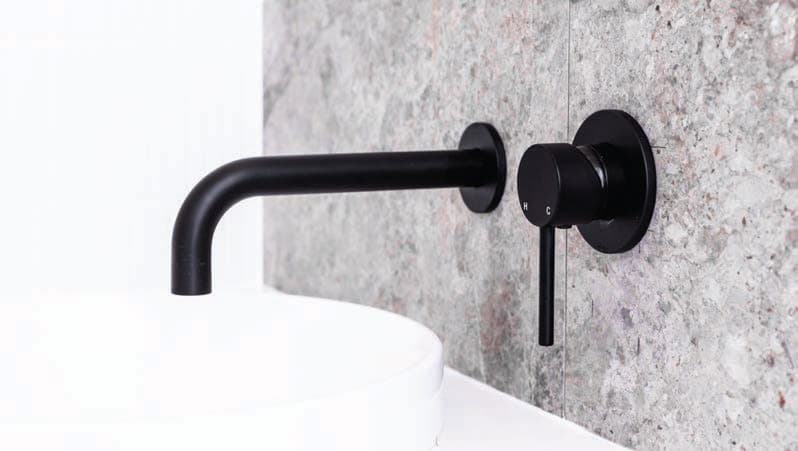 Matt black wall-mounted basin mixer on a stone-tiled wall