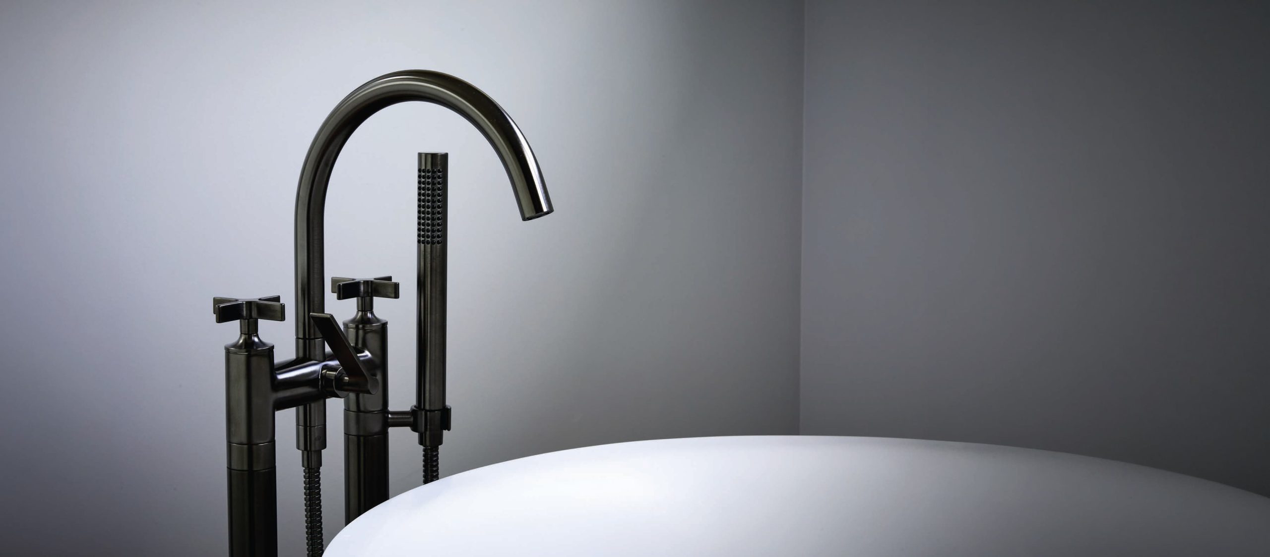 Matt black freestanding bath mixer with hand shower beside a white bath